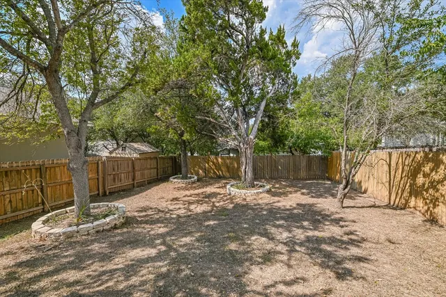 a backyard of a house with large trees and wooden fence