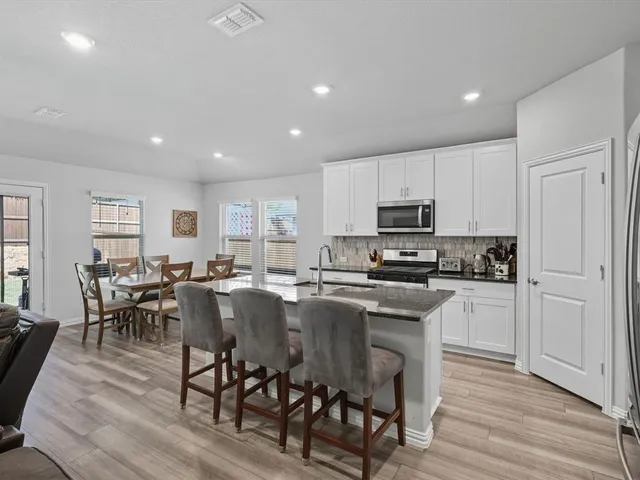 a kitchen with microwave a sink dishwasher a dining table and chairs with wooden floor