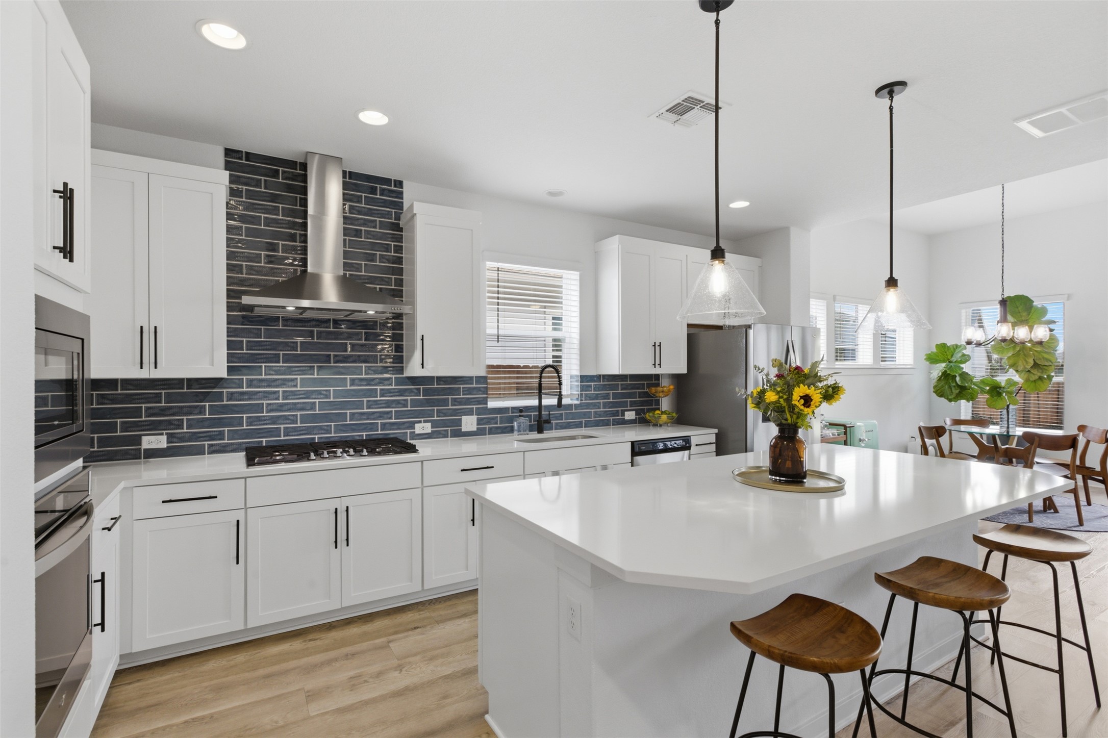 9001 Spire View Austin, TX 78744 - Photo 10 of 35 Kitchen featuring white cabinetry, stainless steel appliances, a dark blue subway tile backsplash, light countertops, and wood-finish flooring