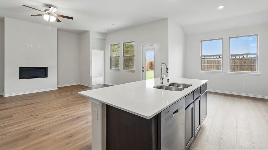 4162 Waldron Trail Forney, TX 75126 - Photo 9 of 29 Open-concept living space featuring wood-finish flooring, an island with a dual basin sink, a built-in fireplace, a ceiling fan, and multiple windows for abundant natural light