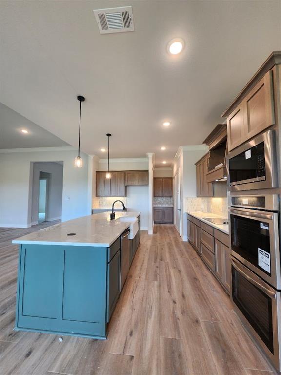 2305 Gypsum Street Krum, TX 76249 - Photo 12 of 22 Open-concept kitchen featuring a large central island with a farmhouse sink, stainless steel appliances including double ovens, wood-finish flooring, recessed lighting, and pendant light fixtures