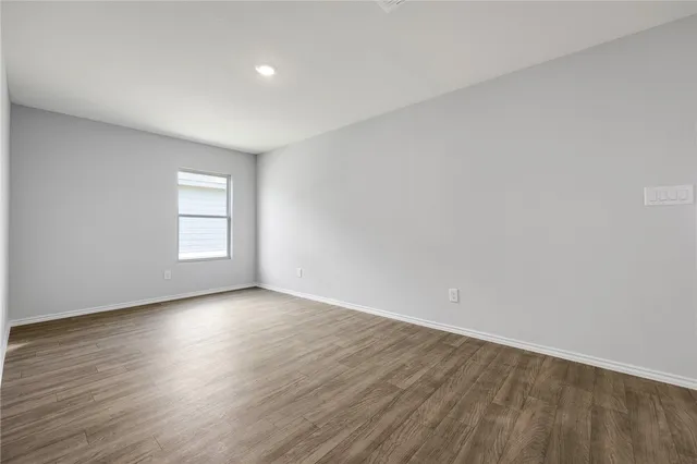 a view of an empty room with wooden floor and window