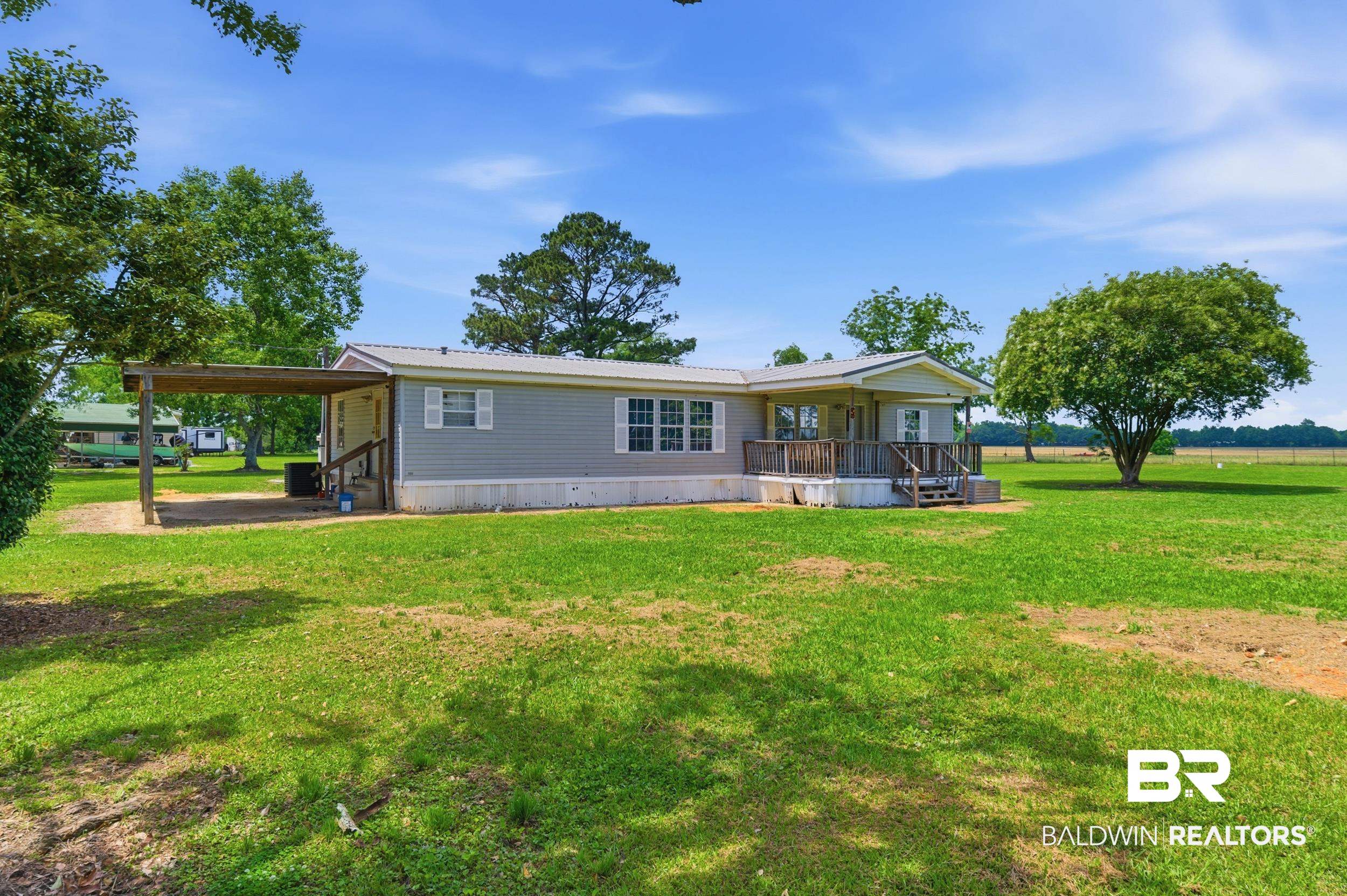926 Tumbling Lane Atmore, AL 36502 - Photo 3 of 56 Single-story home featuring light gray siding, white window shutters, a covered front porch with wood railings, a metal roof, and a covered carport