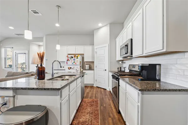 a kitchen with stainless steel appliances granite countertop a stove top oven a refrigerator a sink a dining table and chairs with wooden floor