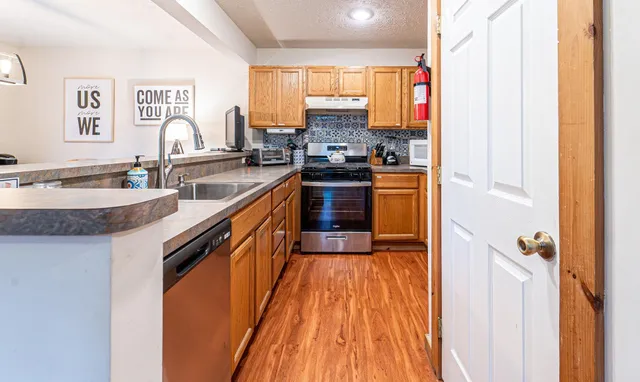 a kitchen with stainless steel appliances granite countertop a refrigerator a sink dishwasher a stove and white countertops with wooden floor