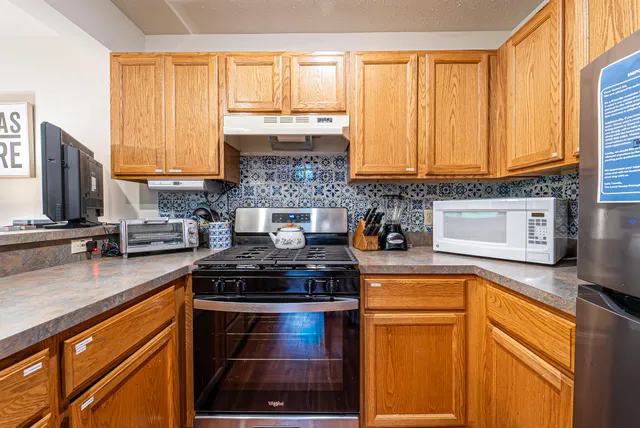 a kitchen with stainless steel appliances granite countertop wooden floors wooden cabinets a sink a stove and a window