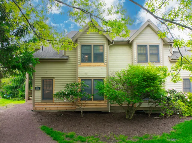 a white house with a big yard plants and large trees