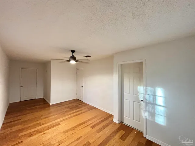a view of empty room with wooden floor and fan