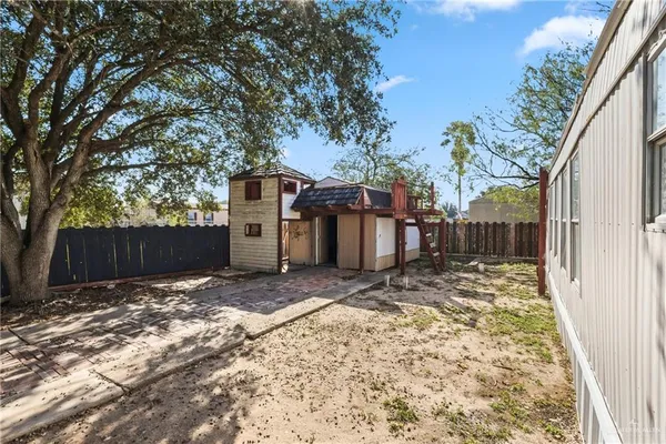 a view of a small yard in front of a house with a large tree and wooden fence