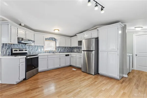 a kitchen with stainless steel appliances granite countertop a refrigerator oven a sink dishwasher and white cabinets with wooden floor