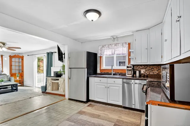 a kitchen with stainless steel appliances kitchen island granite countertop a refrigerator oven a sink dishwasher and white cabinets next to a window