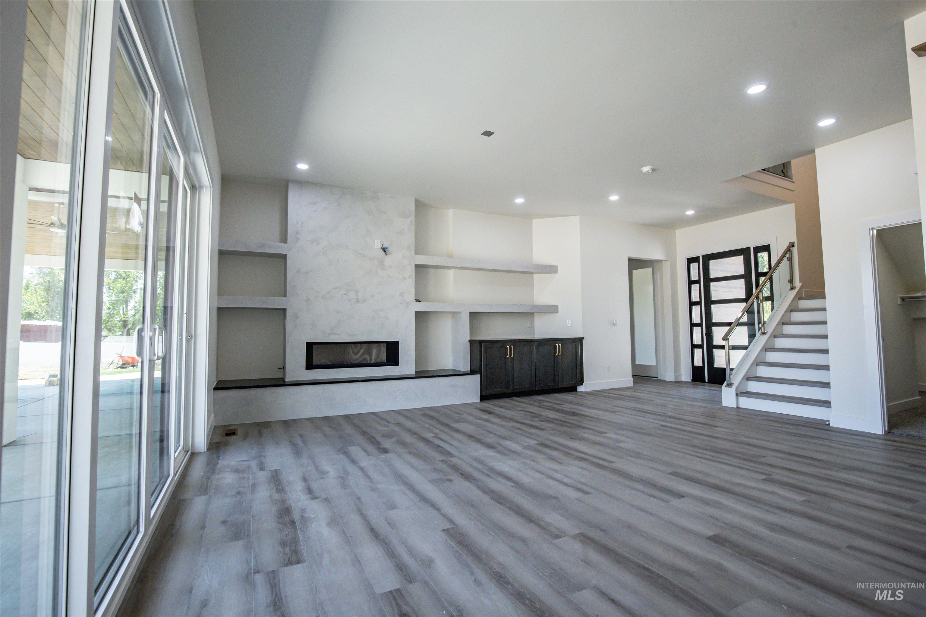 23904 Southview Lane Middleton, ID 83644 - Photo 4 of 29 Spacious interior featuring wide plank wood-finish flooring, a modern fireplace with a stone-finish surround, built-in shelving, sliding glass doors, and a staircase with a glass panel railing