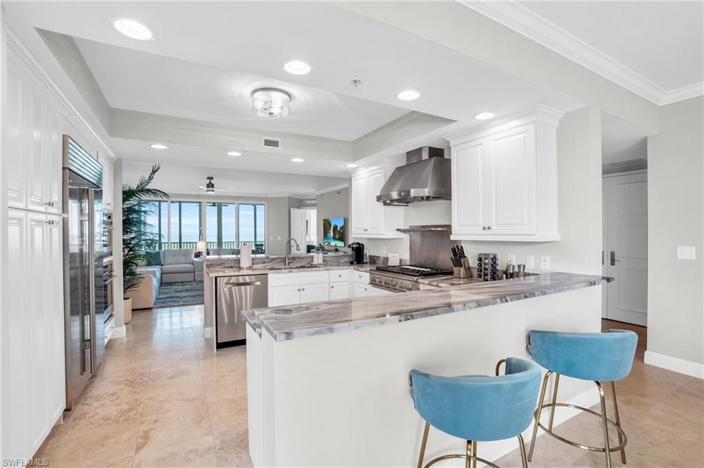 265 Indies Way, Unit 1404 Naples, FL 34110 - Photo 11 of 42 Kitchen with white cabinetry, kitchen peninsula, wall chimney range hood, and stainless steel appliances