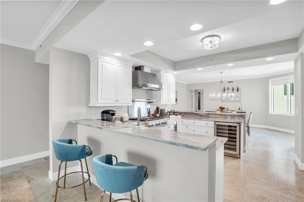 265 Indies Way, Unit 1404 Naples, FL 34110 - Photo 12 of 42 Kitchen with wine cooler, white cabinets, kitchen peninsula, wall chimney range hood, and light stone countertops