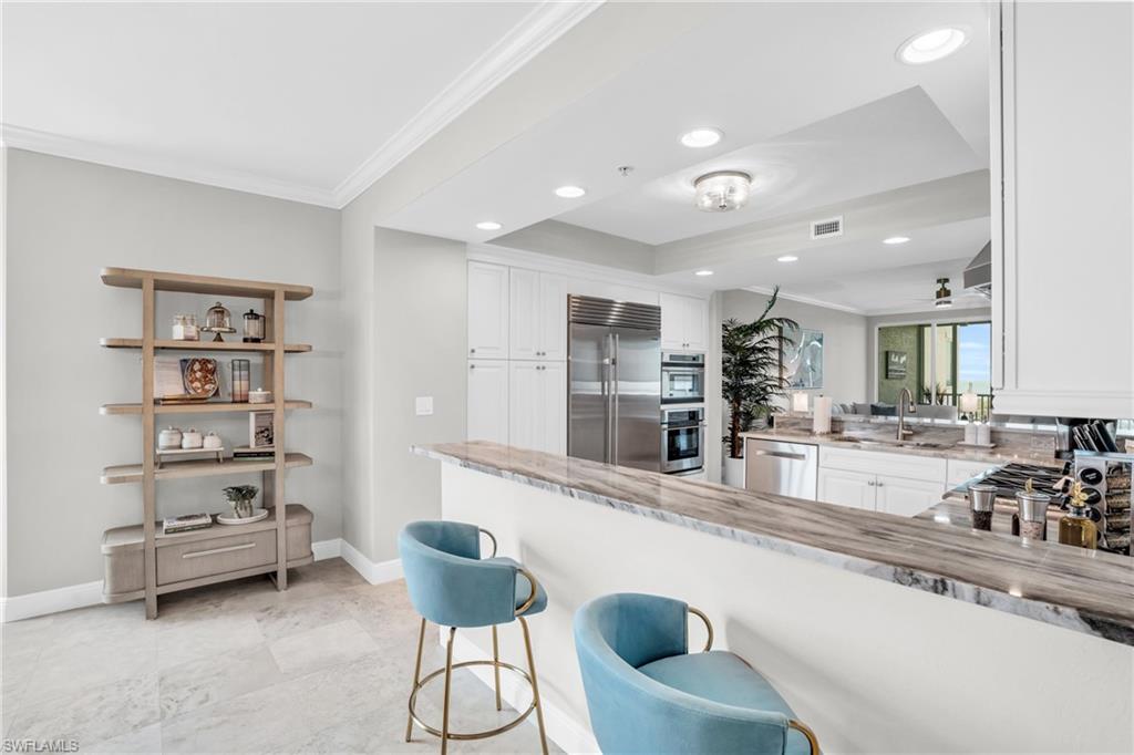 265 Indies Way, Unit 1404 Naples, FL 34110 - Photo 7 of 42 Kitchen featuring stainless steel appliances, kitchen peninsula, light tile patterned floors, white cabinetry, and ornamental molding