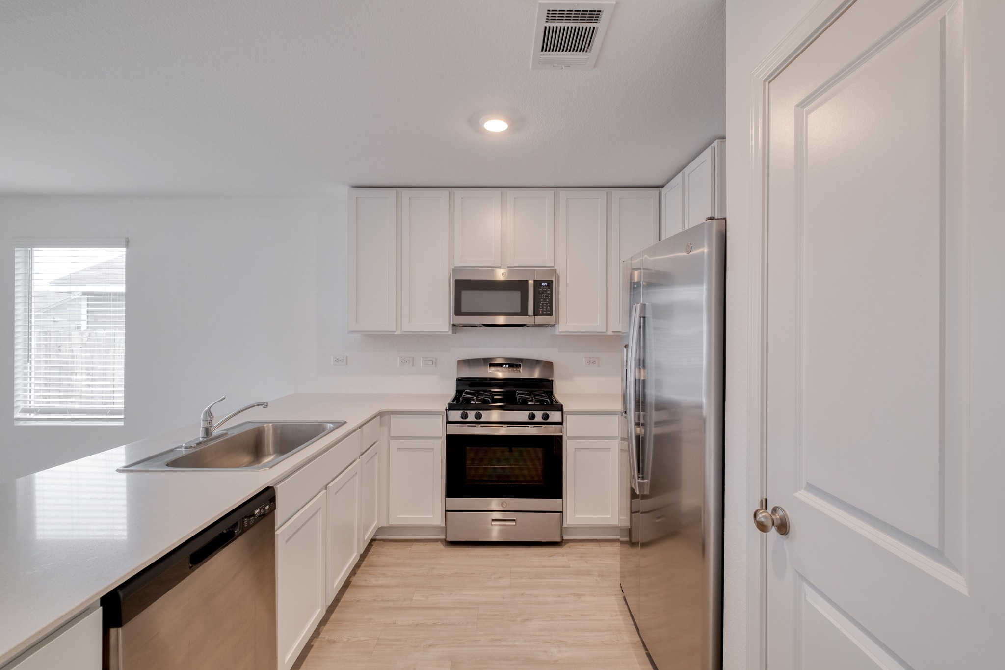 23412 Tiny Moons Way Elgin, TX 78621 - Photo 5 of 38 Kitchen featuring white cabinetry, light countertops, stainless steel appliances, a double basin sink, and wood-finish flooring