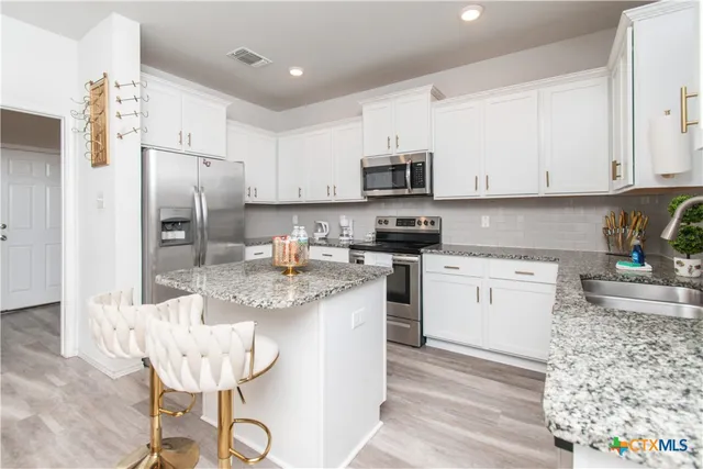 a kitchen with stainless steel appliances granite countertop a stove a refrigerator a sink a stove a dining table and chairs with wooden floor