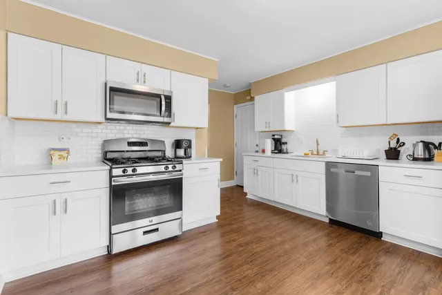 a kitchen with stainless steel appliances white cabinets a sink a stove a microwave and wooden floors