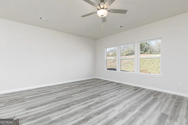 an empty room with wooden floor fan and windows