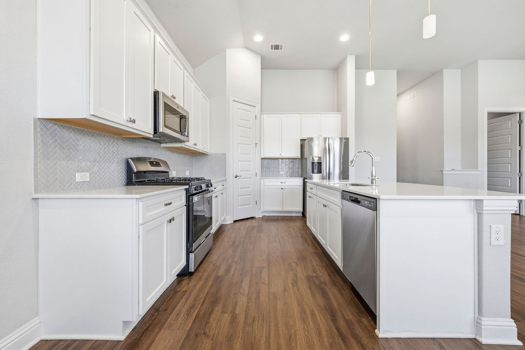 2032 Base Burner Path Leander, TX 78641 - Photo 4 of 34 Contemporary kitchen featuring white cabinetry, stainless steel appliances, light-toned countertops, a herringbone tile backsplash, and wood-finish flooring