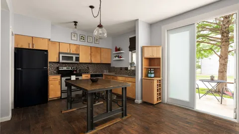 a kitchen with stainless steel appliances granite countertop a refrigerator a sink dishwasher a stove and a dining table with wooden floor