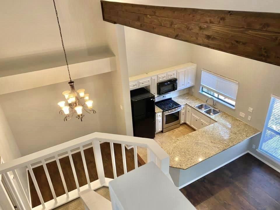 4404 Travis Country Circle, Unit G4 Austin, TX 78735 - Photo 2 of 15 Overlooking a well-appointed kitchen, an open-concept living area features a grand wooden beam and a sophisticated chandelier.