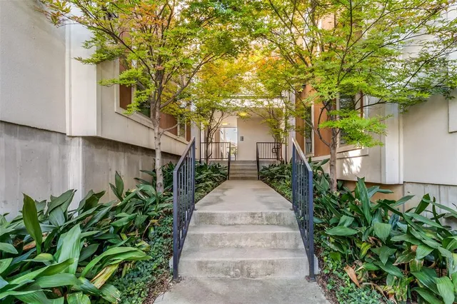 a pathway of a house with potted plants and large trees