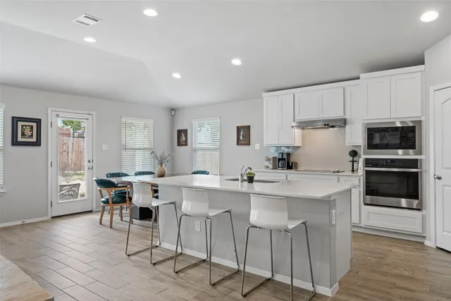 a kitchen with stainless steel appliances a table chairs sink and cabinets