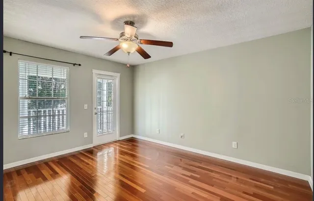 an empty room with wooden floor fan and windows