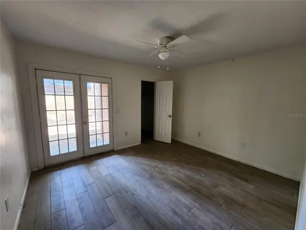 an empty room with wooden floor chandelier fan and windows