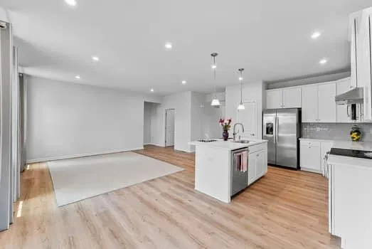 a kitchen with granite countertop a refrigerator a stove a sink dishwasher a refrigerator and white cabinets with wooden floor