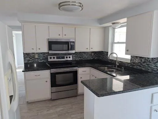 a kitchen with granite countertop a sink stove and microwave