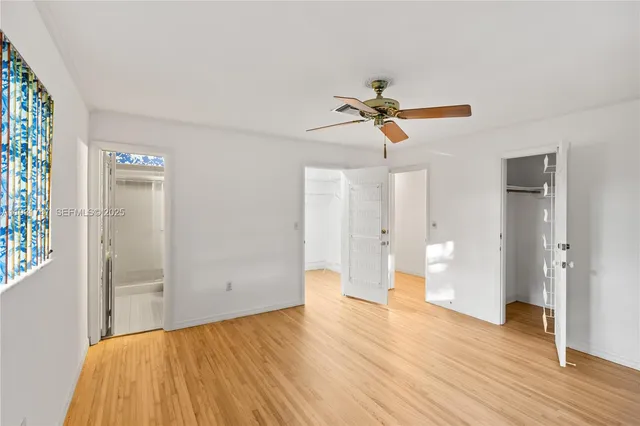 an empty room with wooden floor ceiling fan and windows