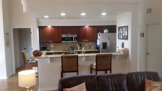 a kitchen with kitchen island stainless steel appliances a sink a stove a refrigerator cabinets and a dining table