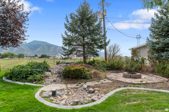 1501 West Elk Circle Mapleton, UT 84664 - Photo 9 of 39 Expansive backyard featuring a stone-lined fire pit area, mature evergreen trees, and a decorative rock garden with concrete edging