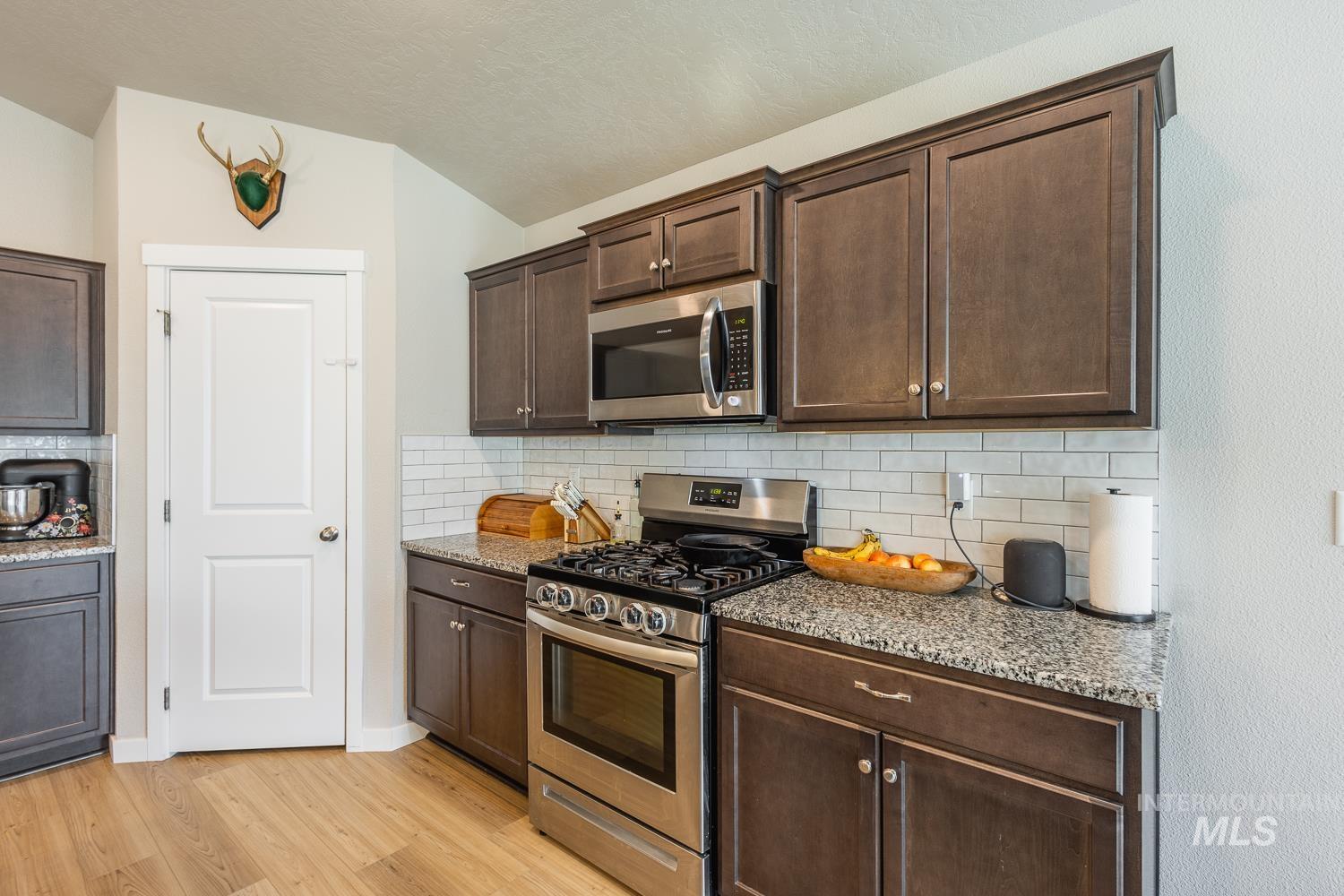 12623 Shadow Peak Street Caldwell, ID 83607 - Photo 20 of 50 Kitchen featuring dark wood-finish cabinetry, granite-style countertops, subway tile backsplash, stainless steel appliances, and wood-finish flooring