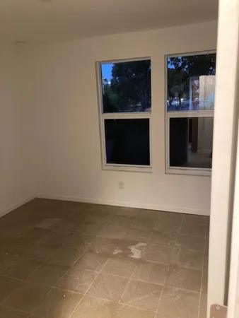 a view of an empty room with kitchen and window