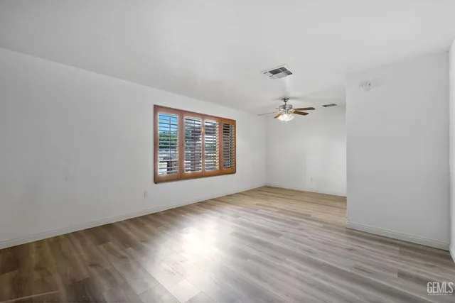 an empty room with wooden floor chandelier fan and windows