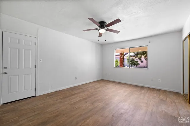 an empty room with wooden floor ceiling fan and windows