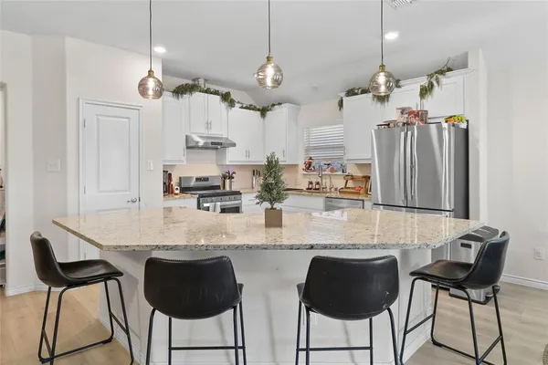 a kitchen with stainless steel appliances kitchen island granite countertop a table chairs and a refrigerator