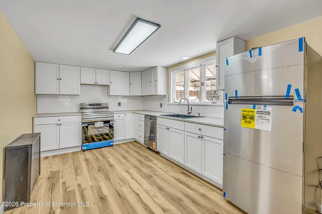 a kitchen with a refrigerator a stove a sink dishwasher and white cabinets with wooden floor