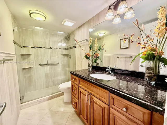 a bathroom with a granite countertop sink a toilet a mirror and shower