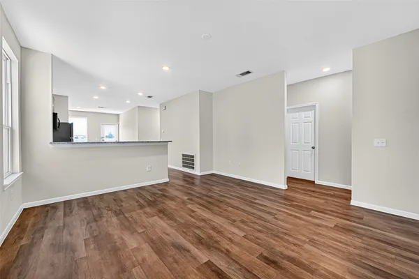 a view of an empty room with wooden floor and kitchen
