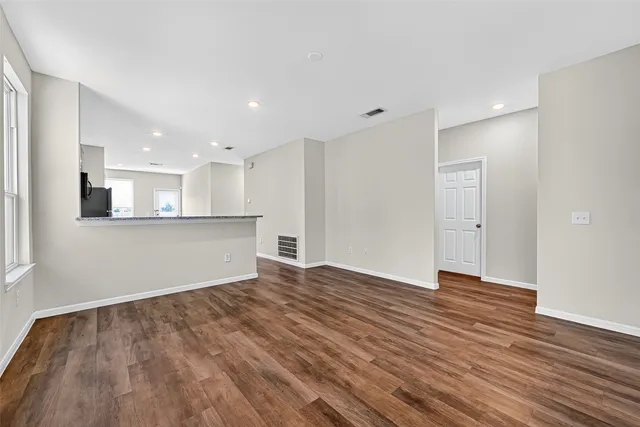 a view of an empty room with wooden floor and kitchen