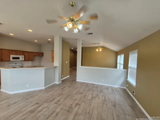 a view of an empty room and kitchen with wooden floor and kitchen space