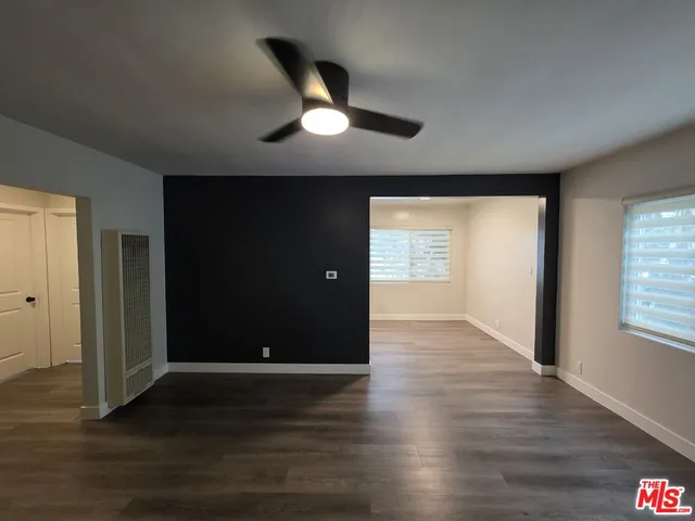 a view of an empty room and kitchen with wooden floor