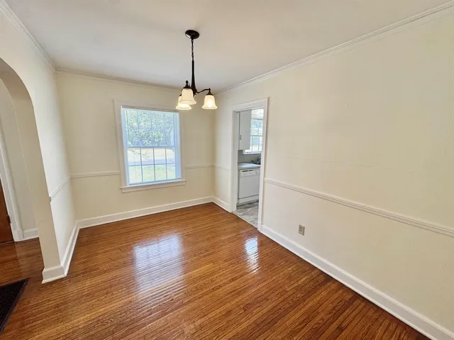 an empty room with wooden floor chandelier and windows