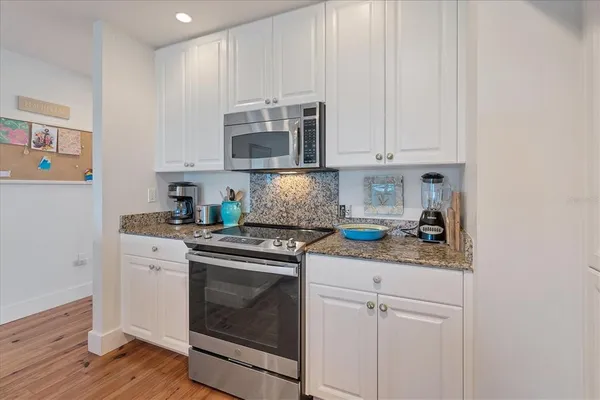 a kitchen with stainless steel appliances granite countertop white cabinets and a stove with wooden floor