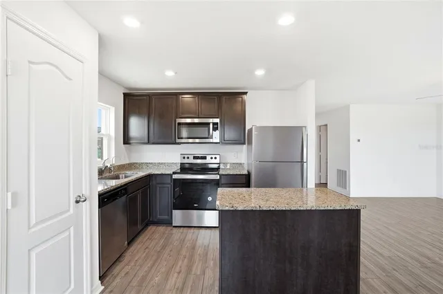 a kitchen with stainless steel appliances granite countertop a stove top oven a sink dishwasher a refrigerator and cabinets with wooden floor