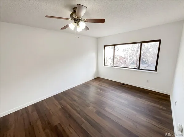 an empty room with wooden floor chandelier fan and windows